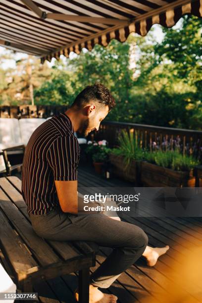 full length of man using smart phone while sitting on bench at back yard - striped awning stock pictures, royalty-free photos & images