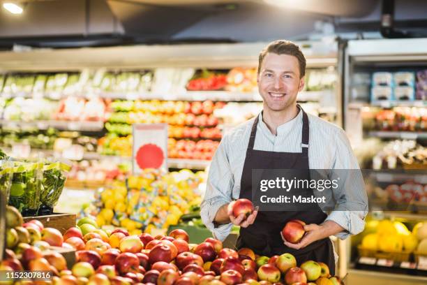 portrait of smiling mature owner standing at apple stall in grocery store - salesman stock pictures, royalty-free photos & images