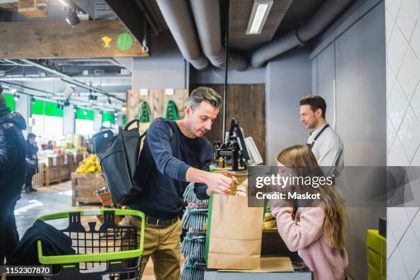 father and daughter packing groceries in paper bag at checkout counter - inserting imagens e fotografias de stock