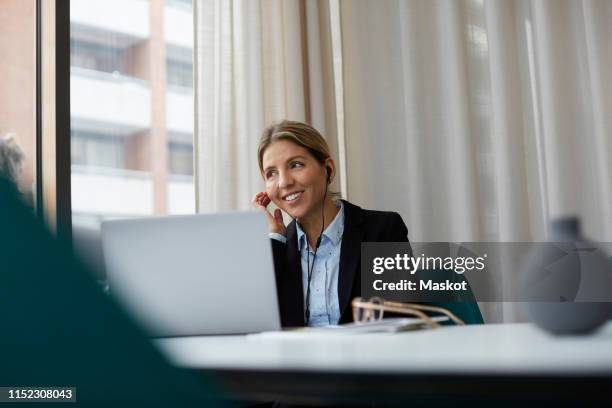 smiling real estate agent talking through headphones while using laptop at estate office - real estate office stockfoto's en -beelden