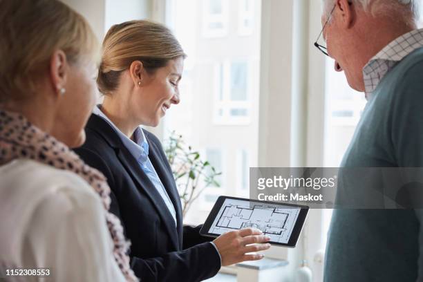 female real estate agent showing new house blueprint on digital tablet to senior couple at home - couple real life stockfoto's en -beelden