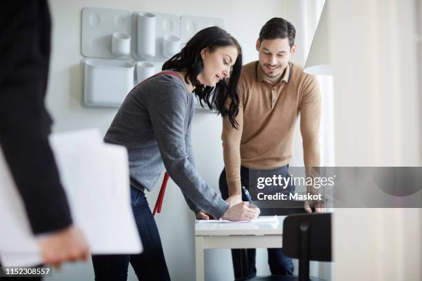 man looking at woman signing papers of new house - man signing paper stock pictures, royalty-free photos & images