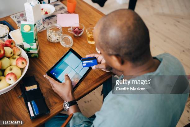 high angle view of man shopping online on digital tablet through credit card in dining room at home - apple credit card stock pictures, royalty-free photos & images