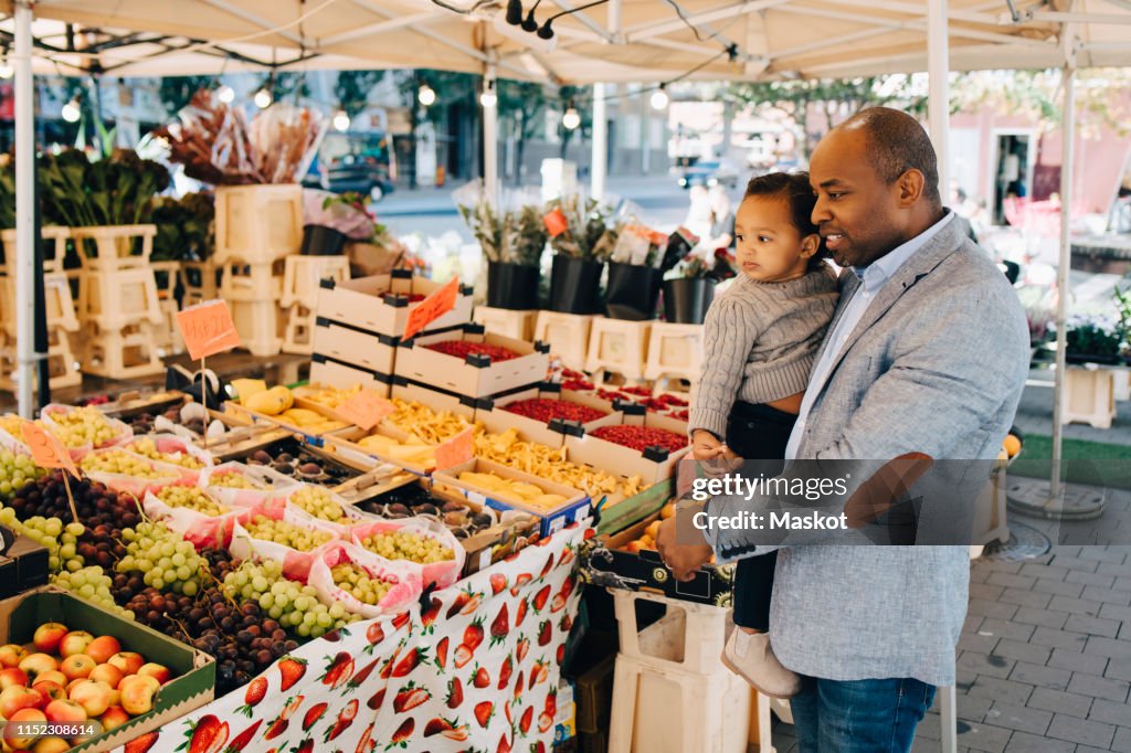 Father carrying daughter while buying fruit and vegetables in market