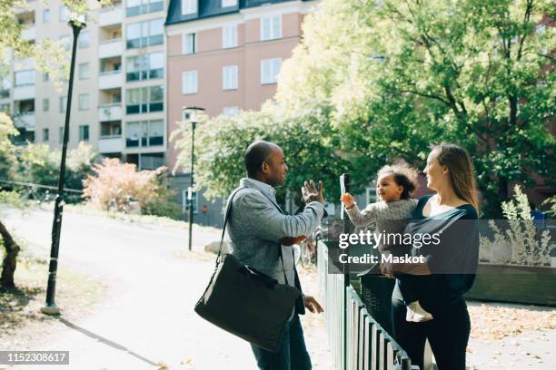 mother carrying daughter waving father at park in city - leaving city stock pictures, royalty-free photos & images