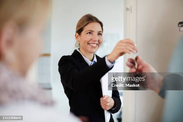 confident smiling real estate agent giving house keys to couple - real estate agent stock pictures, royalty-free photos & images