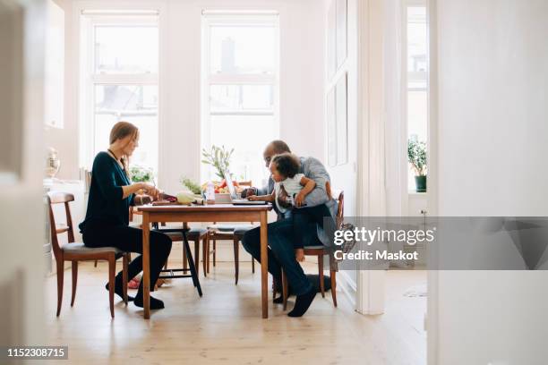 father showing laptop to daughter while mother cutting vegetables at table in house - dinnertable stockfoto's en -beelden