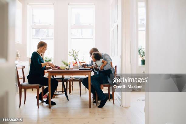father showing laptop to daughter while mother cutting vegetables at table in house - dining table stock pictures, royalty-free photos & images