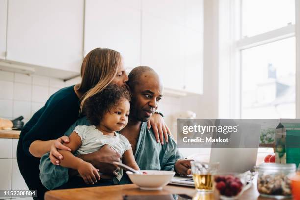 woman embracing and kissing man with daughter using laptop at home - embracing digital stock pictures, royalty-free photos & images