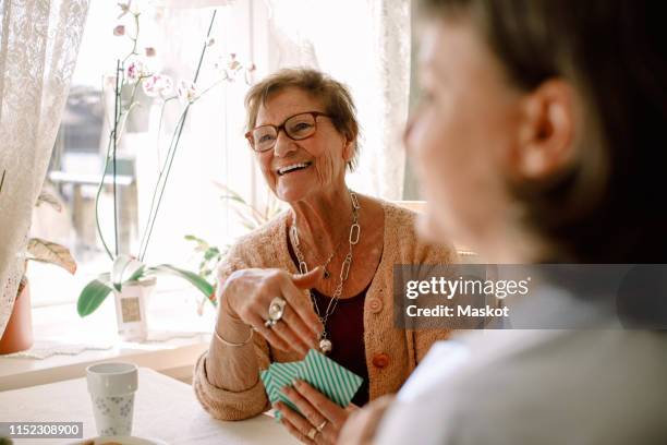 smiling retired senior woman looking away while playing cards with social worker at nursing home - card game mature people stock-fotos und bilder