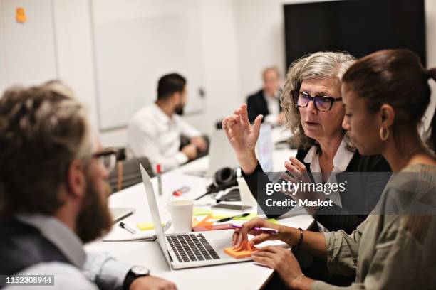 confident mature professional discussing with colleagues in meeting at conference table - 50s woman writing at table imagens e fotografias de stock