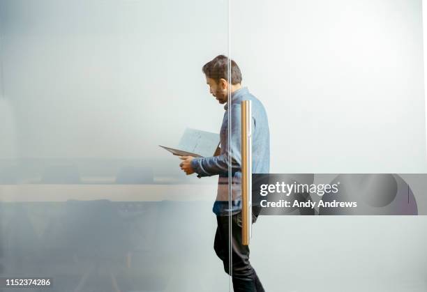 businessman walking in corridor reading notes - office glas stock-fotos und bilder