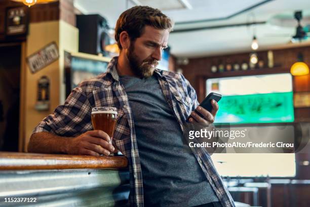 man using smartphone in beer bar - bar man t shirt ストックフォトと画像
