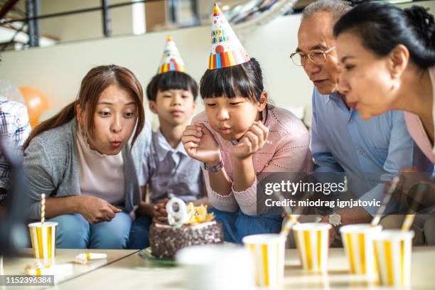 ragazza carina che spegne la candela sulla torta di compleanno con la famiglia - parents children blow candles asians foto e immagini stock