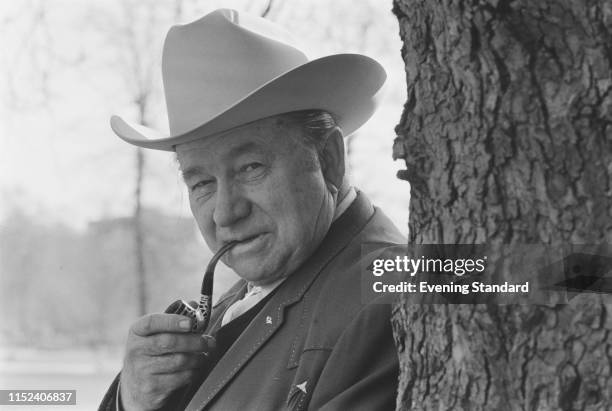 American country music singer and actor Tex Ritter smoking a pipe in a public park, UK, 30th March 1970.