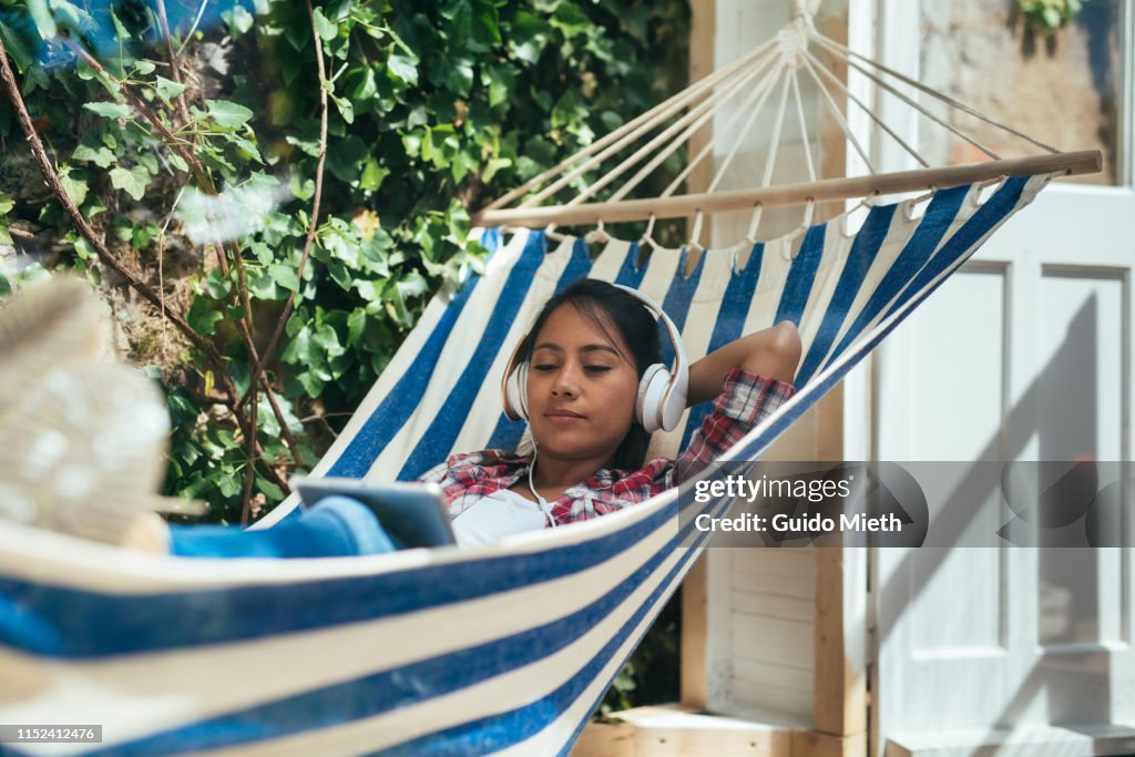 Woman using a tblet pc in hammock while listen to music.