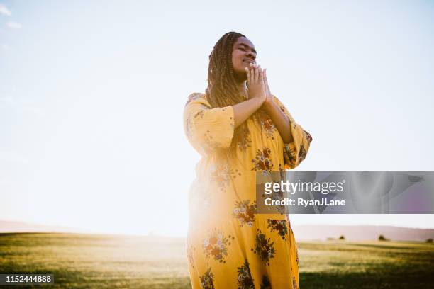 praying african young woman in field - woman praying stock pictures, royalty-free photos & images