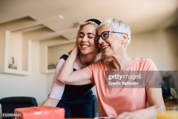 mother hugging her daughter holding a gift - young woman gray hair stock pictures, royalty-free photos & images