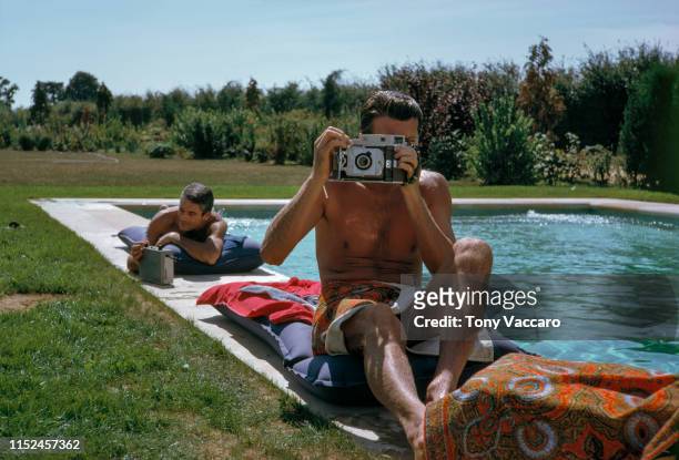 Hubert De Givenchy is sitting by the pool with Philippe Venet at his summer home. Hubert is holding a Polaroid camera and taking picture of Tony...