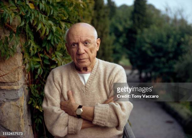 Pablo Picasso standing by a green fern with folded arms, wearing a cashmere sweater.