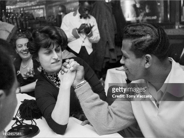 Anna Magnani the Italian actress is arm wrestling Sugar Ray Robinson at his club at Harlem. Around them are people smiling and waitress is standing...