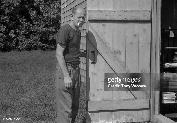 Jackson Pollock holding with his left hand the barn door to his studio at East Hampton; the door is made out of wood and he is smoking a cigarette.