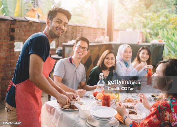 an asian malay chef with apron carving a chicken with friends and family - malay people stock pictures, royalty-free photos & images