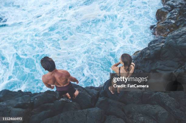 una coppia di millennial si prepara a saltare nell'oceano - tuffi dalle rocce foto e immagini stock