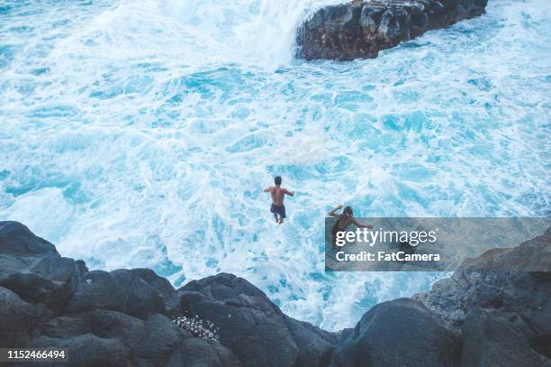 pareja saltando de un acantilado rocoso en el océano para divertirse - salto desde acantilado fotografías e imágenes de stock