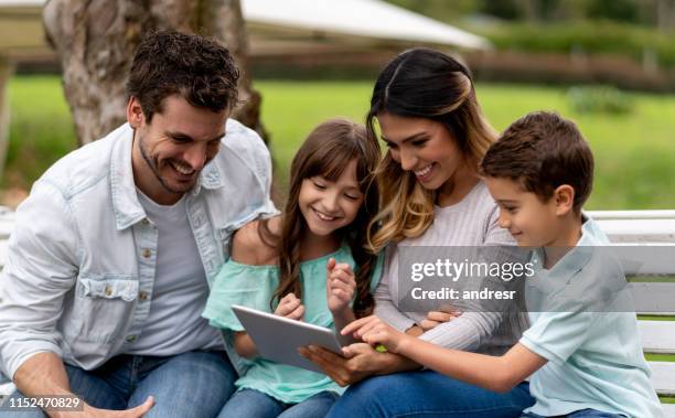 glückliche familie im park mit videos auf tablet-computer - tablet paar sommer stock-fotos und bilder