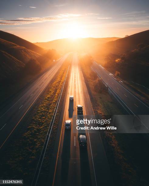 golden light illuminates a remote highway with four cars on it - horizon over land road stock pictures, royalty-free photos & images