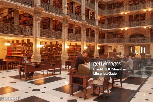 Angled view of patrons looking at books on the ground floor of the George Peabody Library at the Johns Hopkins University, Baltimore, Maryland, June...