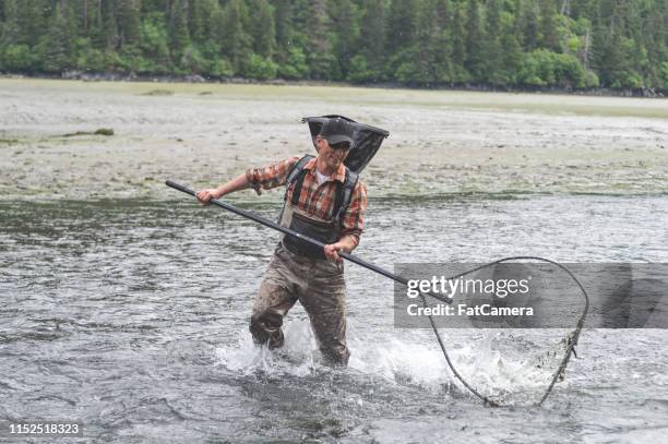 Man Wearing Waders Standing In A River Holding Large Fish Net With
