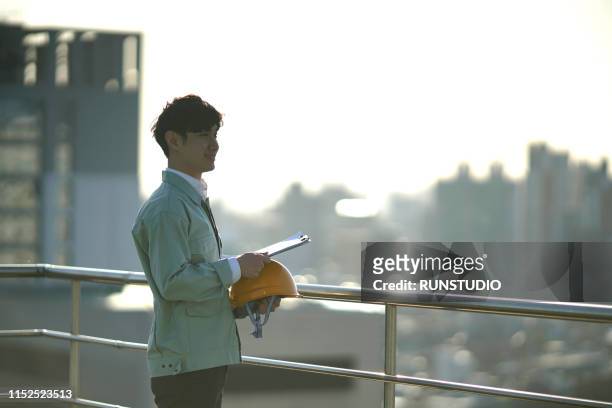 engineer standing with clipboard on rooftop - 工事　日本人 ストックフォトと画像