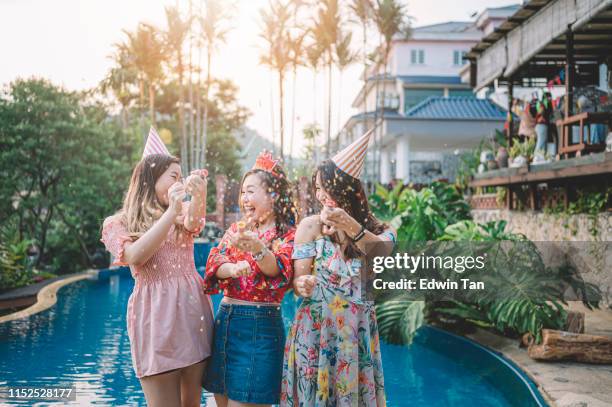 3 aziatische chinese vrouwelijke spelen met confetti aan het zwembad van de achtertuin van het huis tijdens de verjaardag feest evenement in de avond - chinese birthday stockfoto's en -beelden