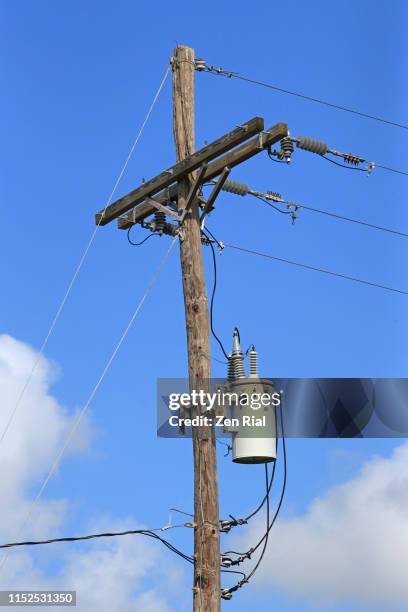 electricity transformer and power cables on a wooden post against blue sky - transformer ストックフォトと画像