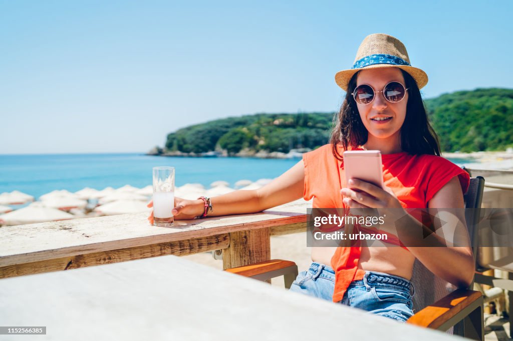 Woman drinking and texting on beach terrace
