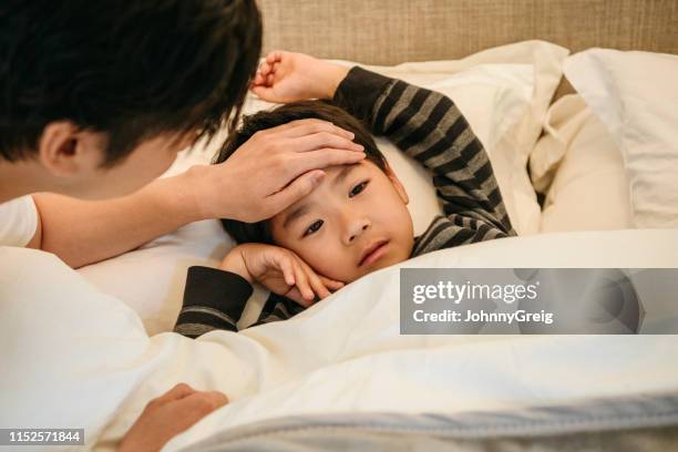 padre comprobando la temperatura del hijo con la mano en la frente - sick kid fotografías e imágenes de stock