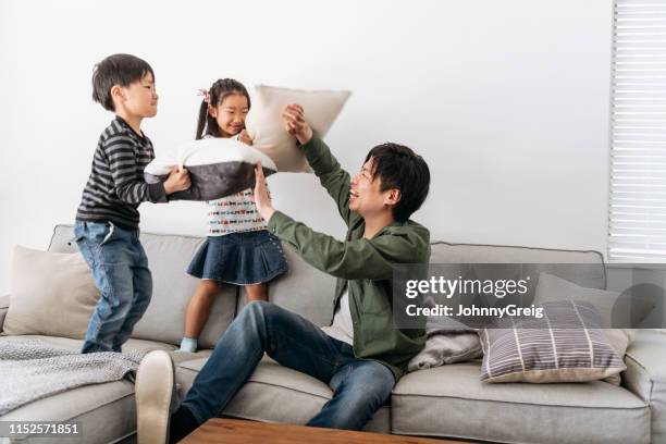 young children having cushion fight on sofa with father - father and child and pillow fight stock pictures, royalty-free photos & images