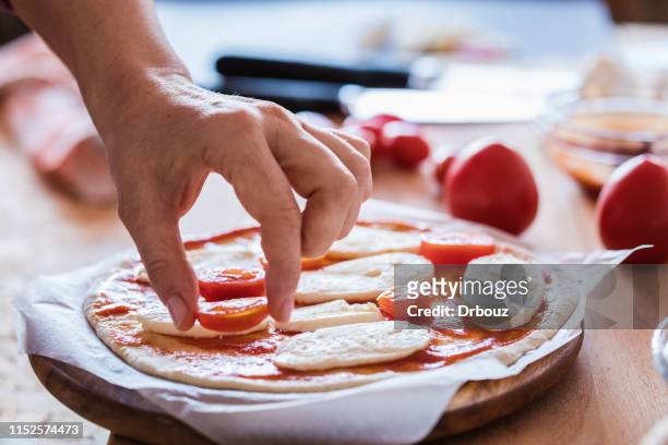 pizza making, mozzarella cheese topping with cherry tomatoes, close-up - pizza ingredients stock pictures, royalty-free photos & images