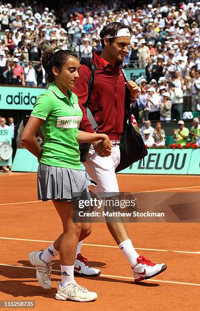 Roger Federer of Switzerland walks out onto the court escorted by a ball girl prior to the men's singles final match between Rafael Nadal of Spain...