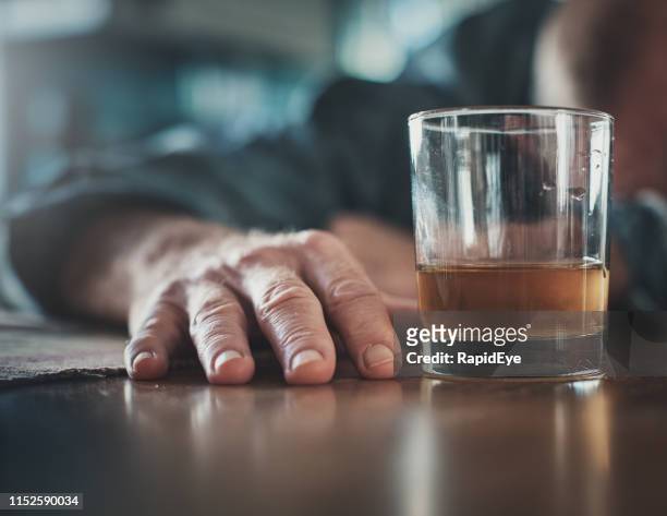 hand by glass of liquor, man's head on table - alcohol abuse stock pictures, royalty-free photos & images