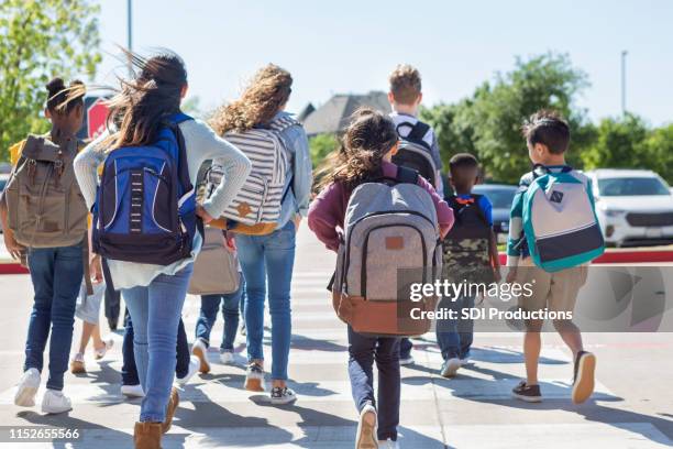 los escolares se alejan de la cámara en crosswalk - backpack fotografías e imágenes de stock