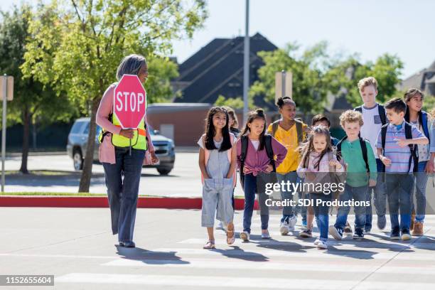 la guardia incrociata femminile conduce i bambini in sicurezza dall'altra parte della strada - attraversamento pedonale foto e immagini stock