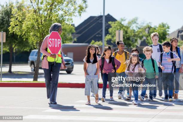 female crossing guard leads children safely across street - the old guard stock pictures, royalty-free photos & images