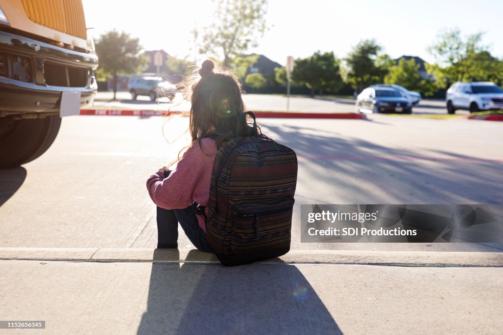Estudante anônima senta-se no meio-fio por ela mesma