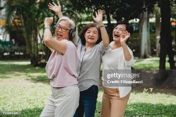 tre damer lyssnar på musik och dansar tillsammans i parken - chinese ethnicity bildbanksfoton och bilder