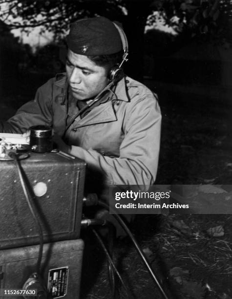 Corporal Lloyd Oliver, a full blooded Native American Navajo, operates a field radio with a Marine artillery regiment somewhere in the South Pacific,...