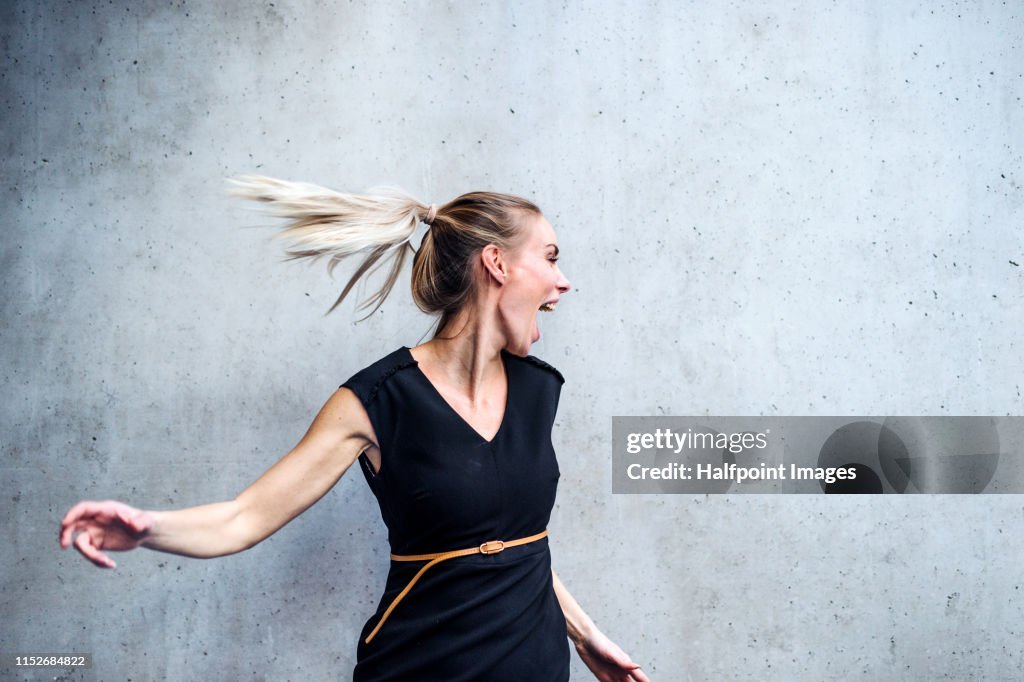 A portrait of businesswoman standing against gray concrete background, having fun.