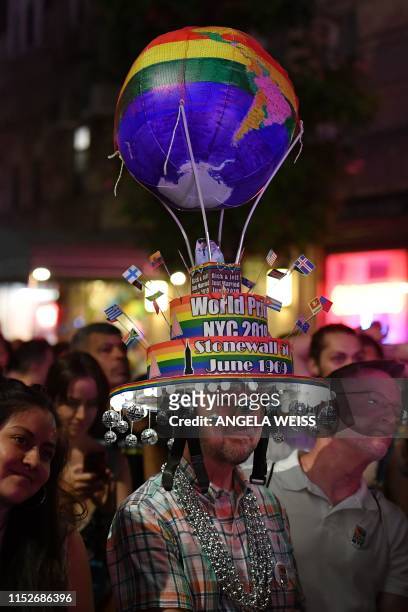 Man wears a hat decorated with a rainbow globe as people gather on Christopher Street outside the Stonewall Inn for a rally to mark the 50th...